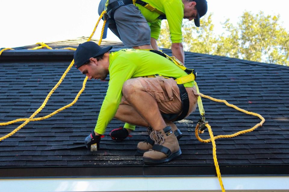 Two roofers working on a shingle roof
